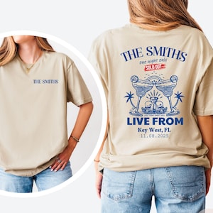 May include: Sand-colored t-shirt with the text "THE SMITHS" on the front and back. The back features a blue graphic of two margarita glasses, palm trees, and the text "LIVE FROM Key West, FL 11.08.2025". The words "SOLD OUT" are also visible.