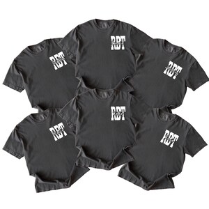 K&ouml;nnte beinhalten: Sechs dunkelgraue T-Shirts mit wei&szlig;em Text. Jedes Shirt hat die Buchstaben "RDT" in einem Blockschrift-Design, mit einem Namen darunter. Die Namen sind Emma, Sophia, Katie und andere. Die Shirts sind kurz&auml;rmlig und haben einen Rundhalsausschnitt.