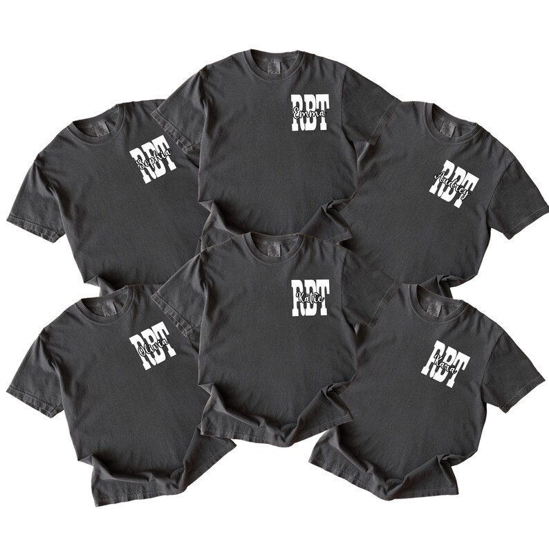 K&ouml;nnte beinhalten: Sechs dunkelgraue T-Shirts mit wei&szlig;em Text. Jedes Shirt hat die Buchstaben "RDT" in einem Blockschrift-Design, mit einem Namen darunter. Die Namen sind Emma, Sophia, Katie und andere. Die Shirts sind kurz&auml;rmlig und haben einen Rundhalsausschnitt.