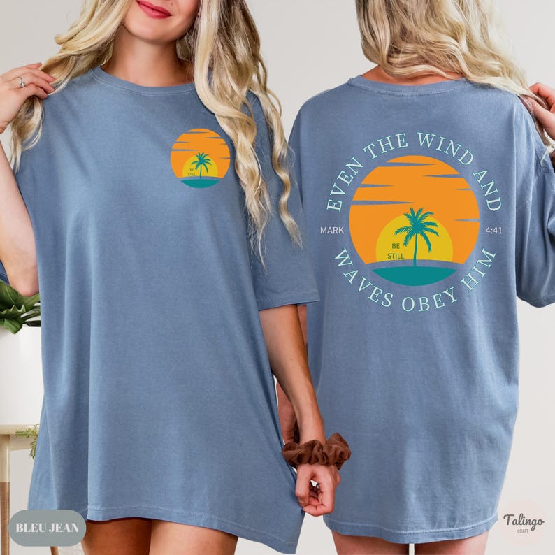 May include: A light blue oversized t-shirt with a graphic of a sunset and palm tree on the front and the text "Even the wind and waves obey him" on the back. The text also includes "Mark 4:41" and "Be Still".