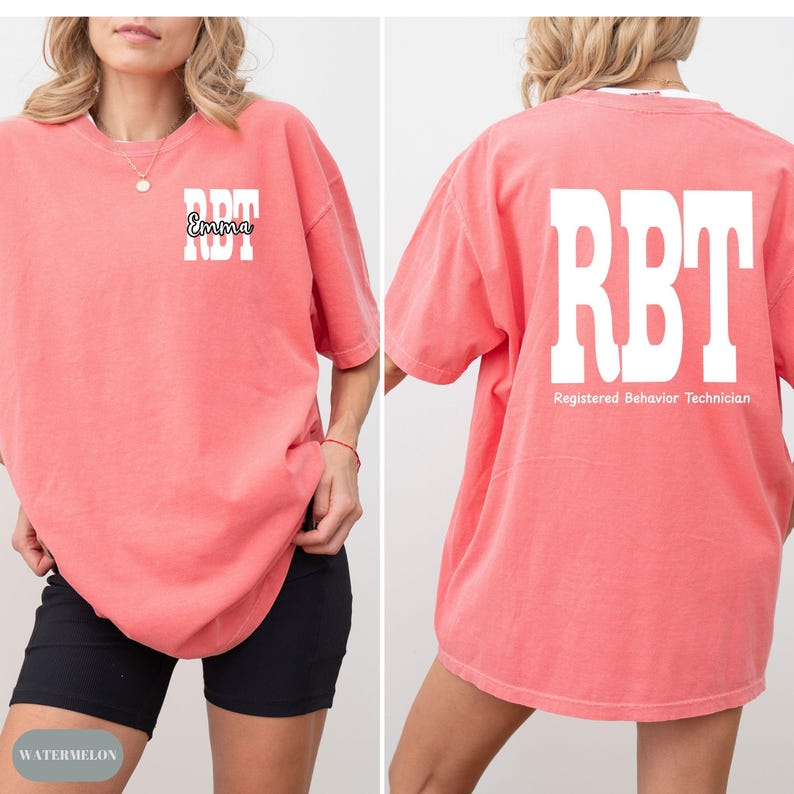 K&ouml;nnte beinhalten: Ein korallenfarbenes T-Shirt mit den Buchstaben "RBT" in Wei&szlig; auf der Vorder- und R&uuml;ckseite. Auf der Vorderseite des Shirts ist auch der Name "Emma" in einer Schreibschrift aufgedruckt. Auf der R&uuml;ckseite des Shirts stehen die Worte "Registered Behavior Technician".