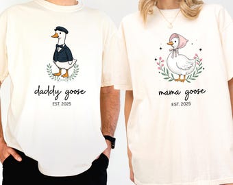 May include: Two ivory t-shirts with a goose graphic and text. The first shirt says "daddy goose est. 2025" and features a goose wearing a bow tie and a top hat. The second shirt says "mama goose est. 2025" and features a goose wearing a pink bonnet.