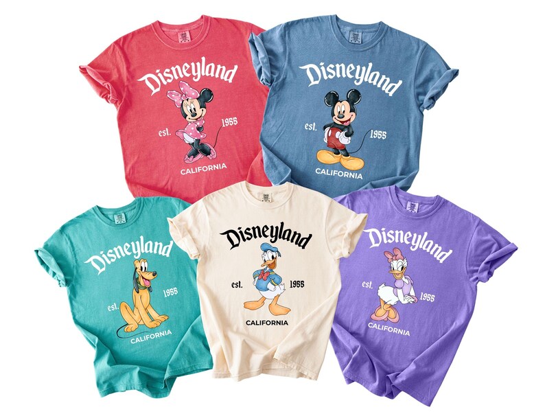 May include: Five colorful t-shirts featuring Disneyland graphics. Each shirt displays a different Disney character: Minnie Mouse, Mickey Mouse, Pluto, Donald Duck, and Daisy Duck. The shirts are in red, blue, teal, cream, and purple.