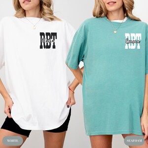 K&ouml;nnte beinhalten: Zwei &uuml;bergro&szlig;e T-Shirts, eines wei&szlig; und eines seegr&uuml;n. Das wei&szlig;e Shirt hat den Text "RBT Olivia" in Schwarz, und das seegr&uuml;ne Shirt hat "RBT Emma" in Wei&szlig;. Die Shirts sind l&auml;ssig und bequem.