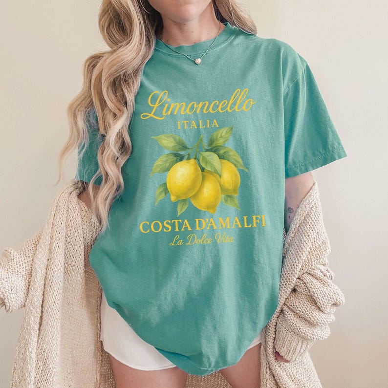 May include: Teal t-shirt with a yellow graphic of lemons and the text "Limoncello Italia Costa D'Amalfi La Dolce Vita". The shirt has a crew neck and short sleeves.