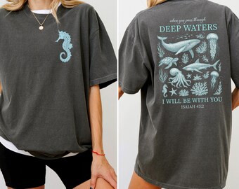 May include: Dark grey t-shirt with a light blue seahorse graphic on the front. The back of the shirt features an ocean-themed design with the text "When you pass through deep waters, I will be with you, Isaiah 43:2."
