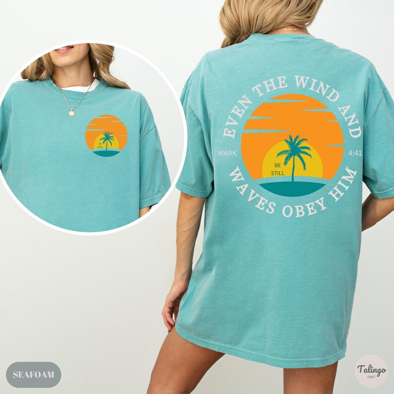 May include: A teal blue t-shirt with a graphic on the back that says "Even the wind and waves obey him" with a sunset and palm tree design. The text "Mark 4:41" is also included. The front of the shirt has a smaller version of the graphic.