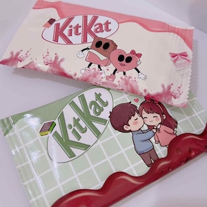 Könnte beinhalten: Zwei Kit Kat-Riegelverpackungen. Eine ist rosa mit Cartoon-Schokoladen- und Herzfiguren. Die andere ist grün mit einem küssenden Cartoon-Paar. Das Kit Kat-Logo ist auf beiden Verpackungen sichtbar.