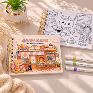 May include: Two spiral-bound coloring books with gold coils. One features a cafe scene with a bear, the text "COZY CAFE," and "Teddy Brew House." The other book has a cat barista and a coffee menu. Three colorful markers are visible.