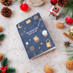 Peut inclure: Un carnet bleu foncé avec le texte "Mon pense-bête pour le net" et diverses illustrations, dont une clé, un cadenas et une enveloppe. Le carnet est entouré de décorations de Noël, dont des pommes de pin et des baies rouges.