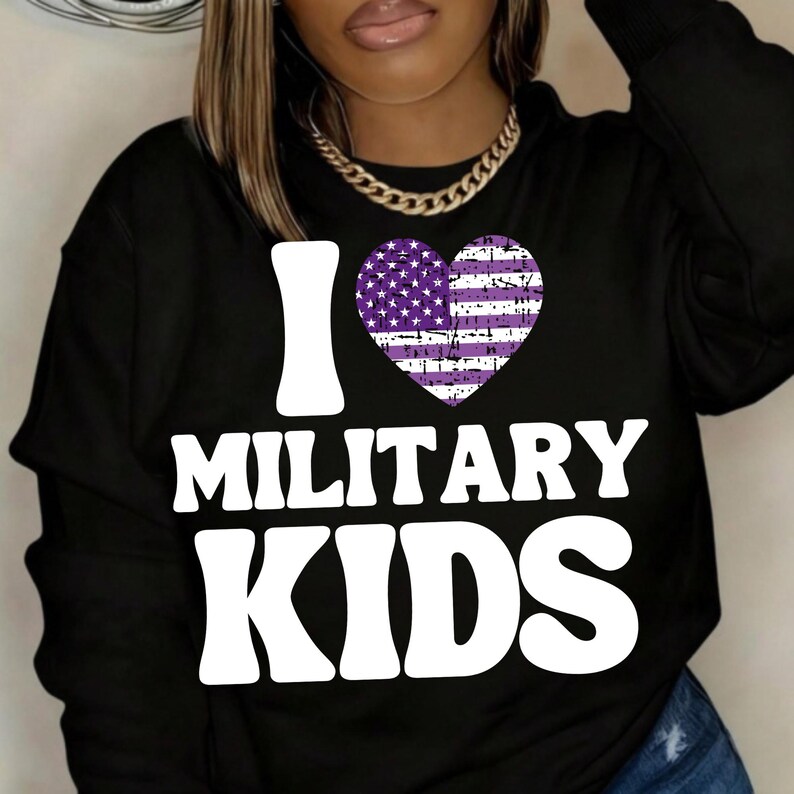 May include: Black sweatshirt with the text "I MILITARY KIDS" in white block letters. A purple heart with a distressed American flag design is centered above the word "MILITARY". The sweatshirt has long sleeves.