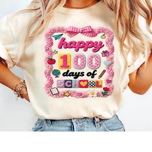 May include: A cream-coloured t-shirt with a pink and white gingham frame. The text reads "happy 100 days of school". The design includes a pink bow, apple, globe, pencil, and other school-themed graphics.