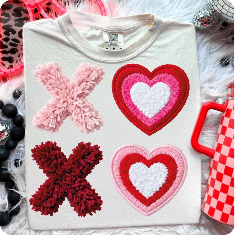 May include: Cream-colored t-shirt with four embroidered patches: two X's and two hearts. The X's are made of fluffy pink and burgundy material. The hearts are layered with white, pink, and red. The shirt has a Comfort Colors tag.
