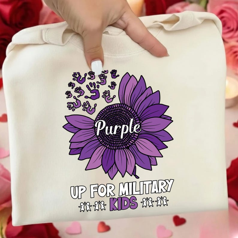 May include: Cream-colored sweatshirt featuring a large purple sunflower with the word "Purple" in the center. Above the sunflower are purple handprints. The text "UP FOR MILITARY KIDS" is printed below the flower.