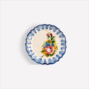 Può includere: Un piatto rotondo in ceramica bianco sporco con un bordo blu smerlato con un motivo floreale. Il centro del piatto mostra un bouquet dipinto a mano di fiori rosa, blu e gialli con foglie verdi. Il piatto ha un diametro di circa 20 cm.