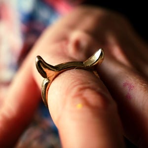 Pode incluir: Um anel dourado com duas pontas de chifres, usado em um dedo.