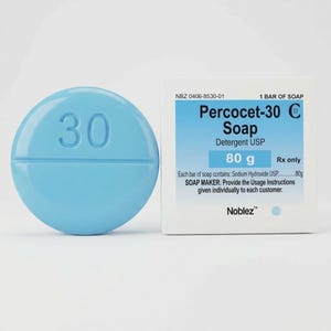May include: A light blue, pill-shaped soap with the number "30" embossed on its surface. Next to it is a white box with the text "Percocet-30 Soap" and "80 g". The soap is a novelty item.