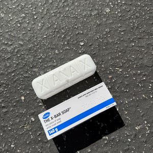 May include: White bar of soap with the word "XANAX" embossed on top. A box of "THE X-BAR SOAP" is next to it, with the text "one piece of soap, white musk smell, 140 g".
