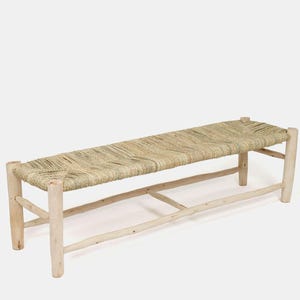 May include: A long, rectangular bench with a woven natural fiber seat and light-colored wooden legs. The bench has a simple, rustic design, perfect for indoor or outdoor use. The bench is approximately 60 inches long.