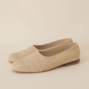 May include: A pair of beige woven flat shoes with a pointed toe. The shoes are made of a natural material and have a simple, elegant design.
