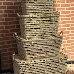 May include: Four natural woven storage baskets stacked on top of each other. The baskets are made of a light brown material and have a rectangular shape. The baskets are all the same size and have a woven pattern.