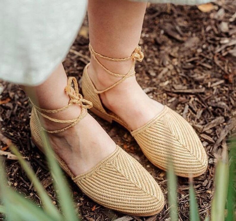 Op de afbeelding: Een paar beige geweven sandalen met enkelbandjes. De sandalen zijn gemaakt van een natuurlijk materiaal en hebben een eenvoudig, elegant ontwerp.