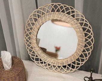 May include: A round woven wicker mirror with a natural wood finish. The mirror has a decorative, intricate design with a circular frame.