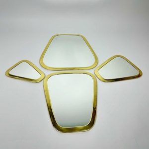 May include: Set of four gold-toned framed mirrors with geometric shapes. The mirrors are arranged in a cluster, with the largest mirror in the centre.