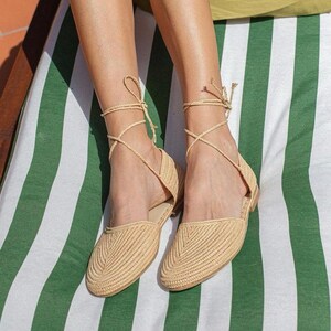 Op de afbeelding: Een paar beige geweven sandalen met vetersluiting. De sandalen zijn gemaakt van natuurlijke materialen en hebben een comfortabele, casual stijl.