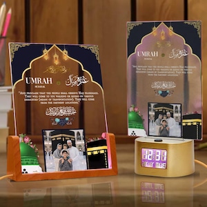 Op de afbeelding: Een gouden digitale klok met een roze display, een bruine houten standaard met een glazen paneel met een afbeelding van de Kaaba en een citaat over de Umrah-pelgrimstocht in het Arabisch en Engels, en een tweede glazen paneel met een afbeelding van een gezin voor de Kaaba.