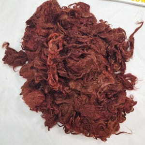 May include: A mass of reddish-brown fibre, possibly wool or a similar material, with a curly, textured appearance. The fibres are densely packed, creating a voluminous mass. The colour varies slightly, with some areas lighter.