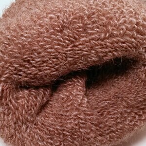 May include: Close-up of a soft, brown, fuzzy yarn. The yarn is tightly wound into a ball shape.