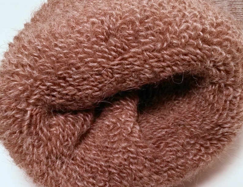 May include: Close-up of a soft, brown, fuzzy yarn. The yarn is tightly wound into a ball shape.