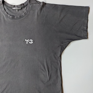 以下が含まれることがあります： クルーネックと半袖のチャコールグレーのTシャツ。胸元には白い「Y-3」のロゴが入っています。Y-3のロゴは、首の後ろのタグにも表示されています。柔らかい素材で作られたTシャツです。
