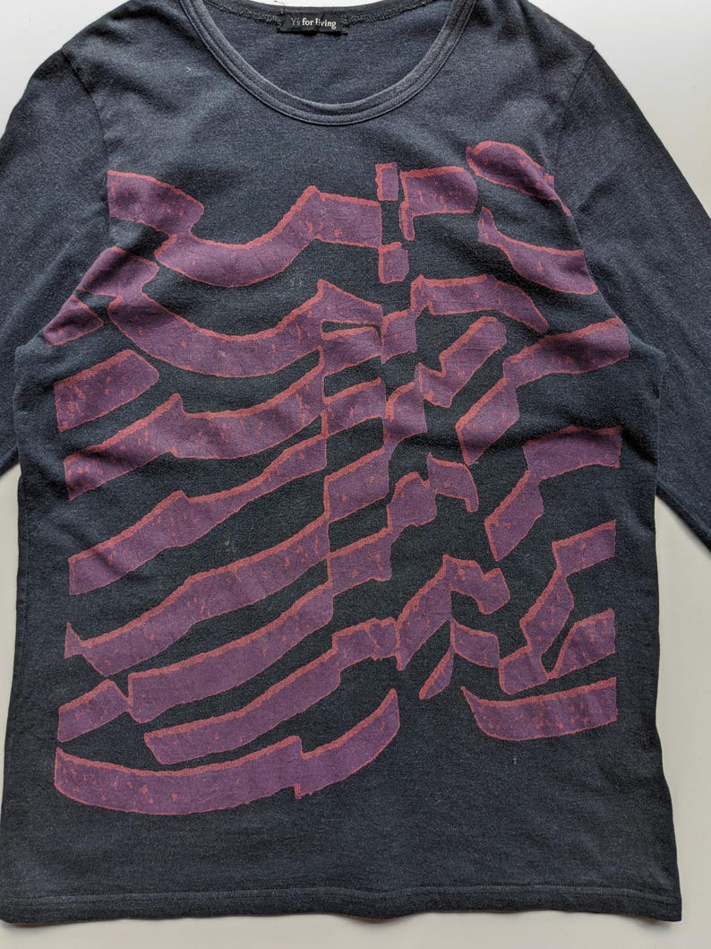 Op de afbeelding: Donkergrijs shirt met lange mouwen, een ronde hals en een groot, abstract ontwerp in paarse tinten. Het ontwerp bestaat uit overlappende, gebogen lijnen. Het shirt is gemaakt van een zacht, comfortabel materiaal.