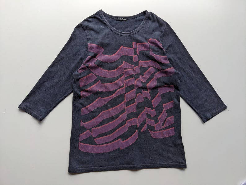 Op de afbeelding: Donkerblauwe longsleeve met een paars ribbenkastontwerp. De shirt heeft een ronde hals en driekwart mouwen. De afbeelding is een gestileerde weergave van een ribbenkast.