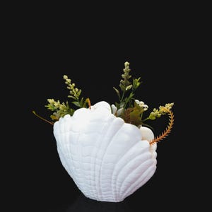 Peut inclure: Un pot en forme de coquille de mer en céramique blanche avec des fleurs vertes et blanches.