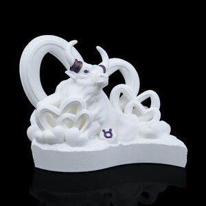 May include: White ceramic figurine of a bull with a purple Taurus symbol. The bull is sitting on a cloud-like base with swirling white details.