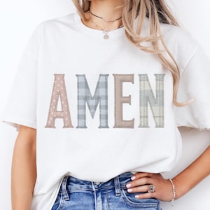 Puede incluir: Camiseta blanca con la palabra "AMEN" en un diseño de patchwork. Las letras están en varios patrones: lunares rosas, cuadros azules y cuadros beige. Una prenda casual para el día a día.