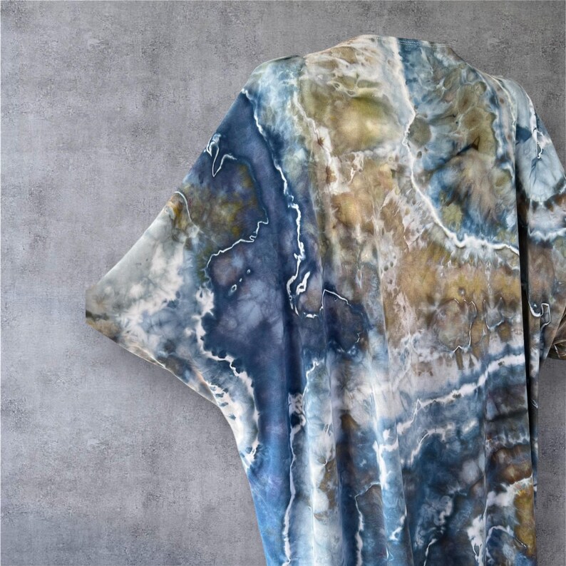 Pode incluir: Um tecido tie-dye azul, marrom e branco com um padr&atilde;o de m&aacute;rmore. O tecido est&aacute; drapeado sobre um fundo cinza.