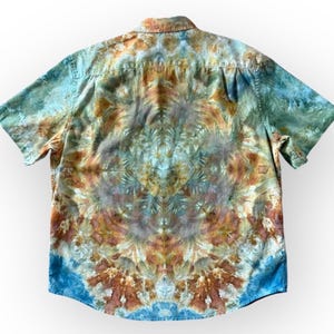 May include: Short-sleeved button-down shirt with a tie-dye pattern in shades of blue, brown, and green. The shirt has a classic collar and a relaxed fit, perfect for casual wear. The tie-dye design creates a unique, artistic look.