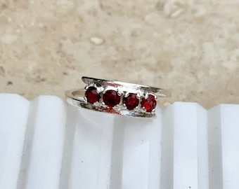 Può includere: Un anello d'argento con cinque pietre preziose rosse incastonate in una fascia.