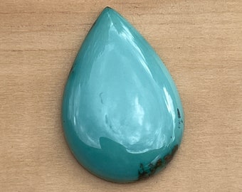 May include: A teardrop-shaped turquoise cabochon with a smooth, polished surface and a light blue color.