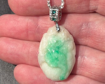 Könnte beinhalten: Ein weißer Jade-Anhänger mit grünen Jade-Akzenten, geschnitzt mit einem floralen Design. Der Anhänger ist an einer silbernen Kette mit einer kleinen diamantbesetzten Öse befestigt.