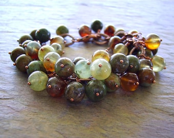Può includere: Un braccialetto avvolto in filo di rame con perline di colore verde, marrone e ambra. Le perline sono raggruppate in una forma a grappolo.