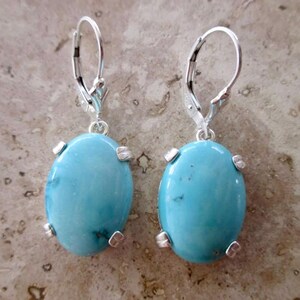 May include: A pair of silver dangle earrings with oval turquoise stones. The stones are a light blue color and have a smooth, polished finish.