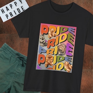 May include: A black t-shirt featuring a graphic print with the word PRIDE repeated in colorful, bubble-style lettering. The design includes several illustrations of brown bears integrated among the letters, set against a gradient background.