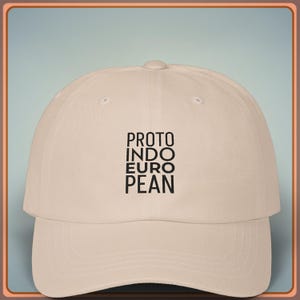 Può includere: Cappellino da baseball beige con visiera curva. Il cappellino presenta il testo "PROTO INDO EURO PEAN" in nero, impilato verticalmente sul davanti. Il cappellino ha un classico design a sei pannelli.