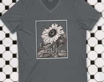 Könnte beinhalten: Ein graues V-Ausschnitt-T-Shirt mit einer schwarz-weißen Sonnenblumenillustration in einem weißen Rahmen. Das Sonnenblumendesign zeigt detaillierte Blütenblätter, Blätter und Stängel. Das Shirt besteht aus einem weichen Material.