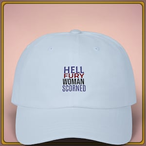 Può includere: Cappellino da baseball azzurro con la scritta ricamata "HELL FURY WOMAN SCORNED" in blu navy, rosso e nero. Il cappellino ha una visiera curva e una corona arrotondata.